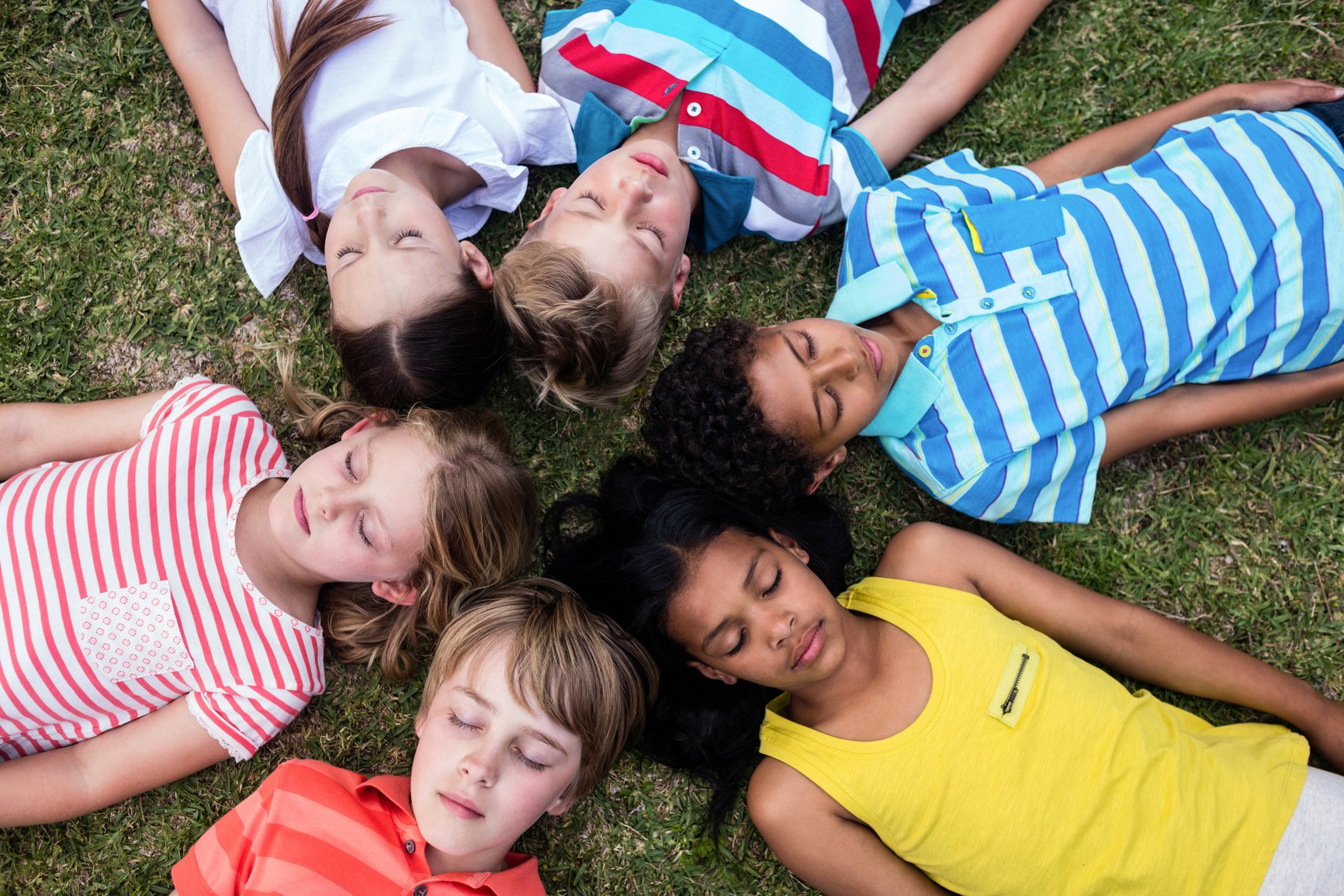 Children lying on grass with eyes closed