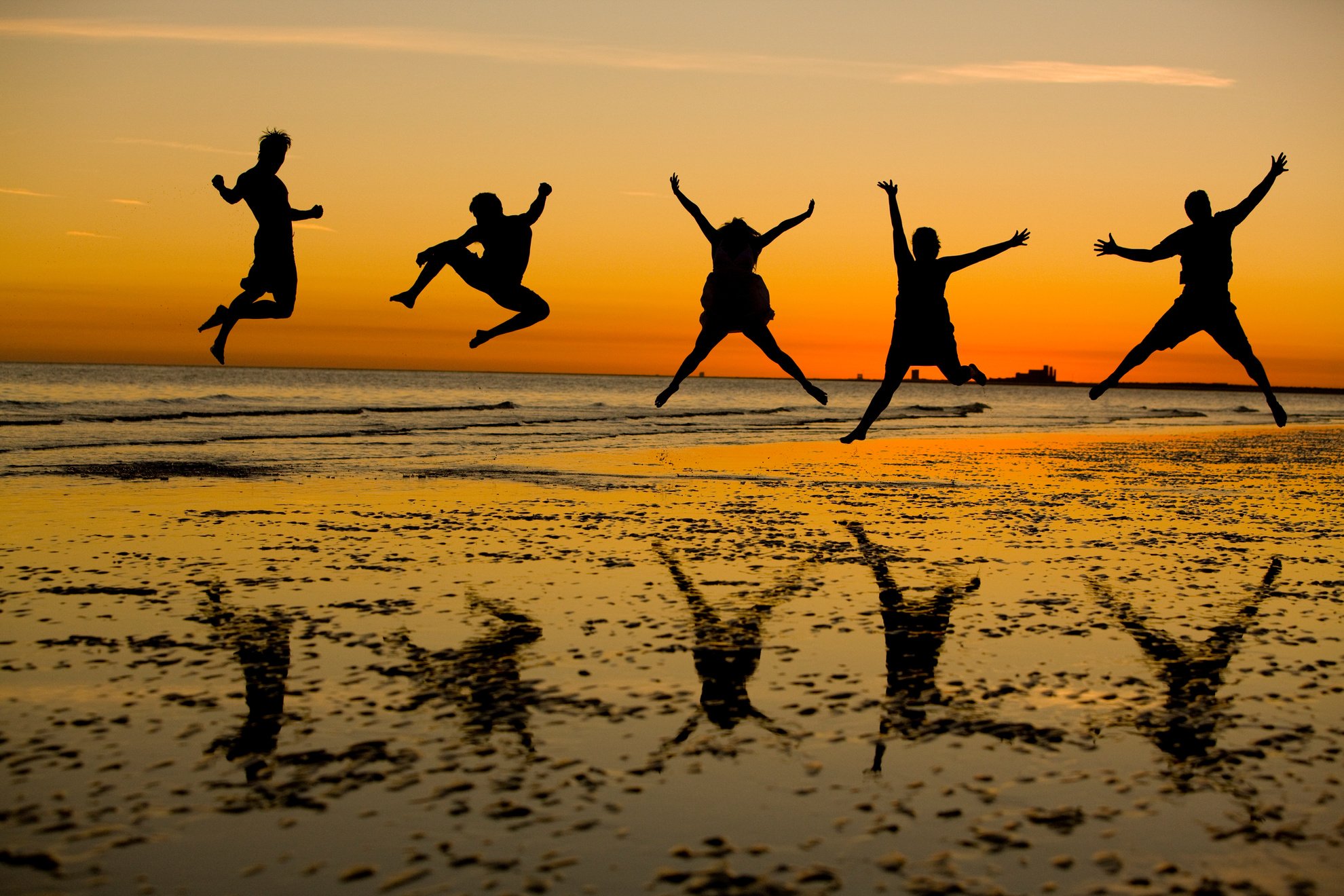 Jumping people on the beach in shadows